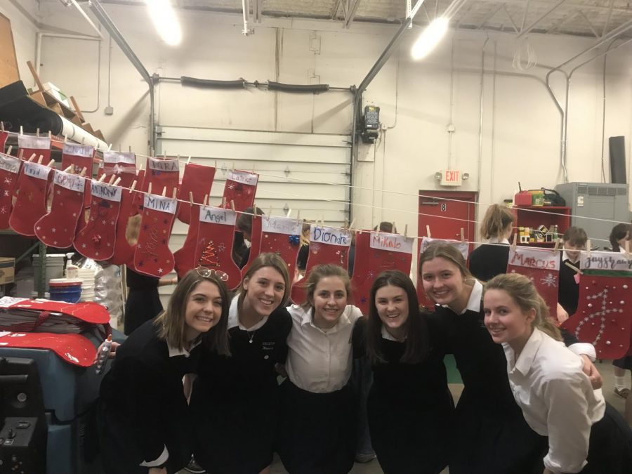 Wini Bettenburg, Maddie Mork, Rachel Coss, Sara Commers, Sadie Grunau, and Nicole Bauman in front of completed  Christmas stockings.